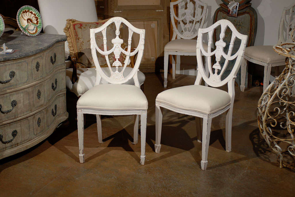 A set of six Danish painted Hepplewhite shield style dining chairs from the 19th century. This set of six dining room chairs was born in 19th century Denmark. Each chair features a carved shield back with urn and swag motifs, typical of the ornate