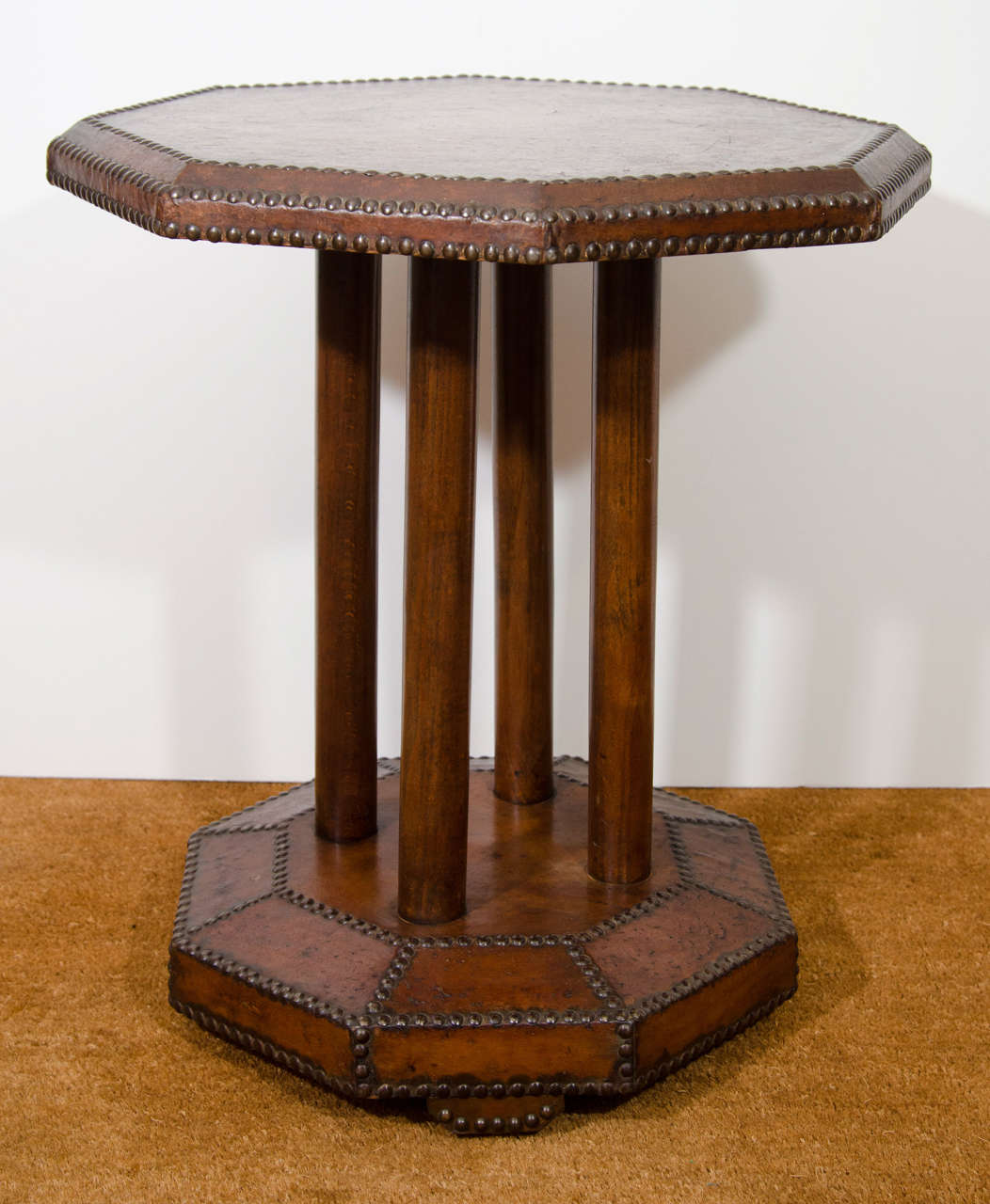 The leather table with octagonal top above 4 wooden cylindar supports, resting on an octagonal base raised on leather block feet, the leather with close-nailed trim/decoration