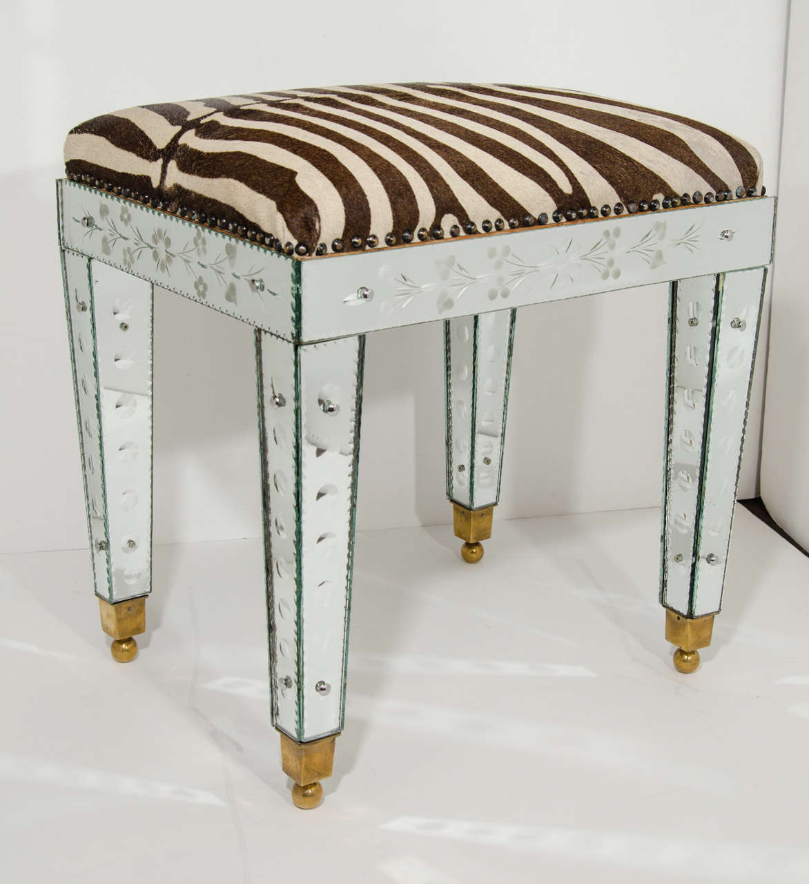 Elegant bench comprised of Venetian mirrored base and upholstered in exotic vintage zebra hide with antique brass stud details. Mirrored base is hand worked with reverse etched floral designs, and features convex circles.  The mirrored panels have
