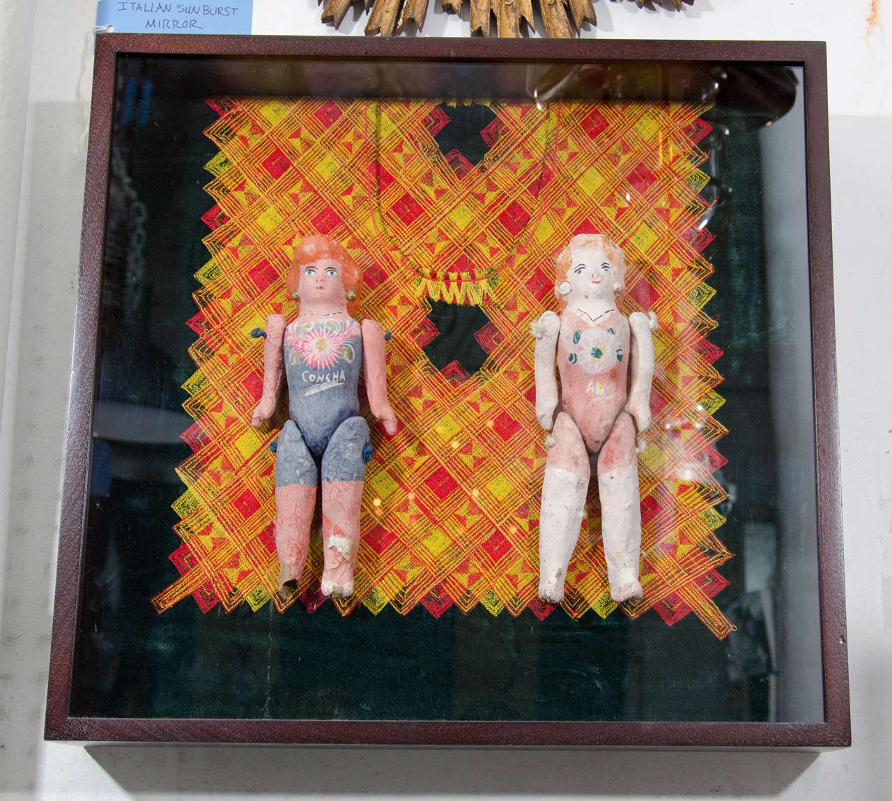 A pair of Mexican papier mâché dolls mounted on velvet huipil in a shadowbox.