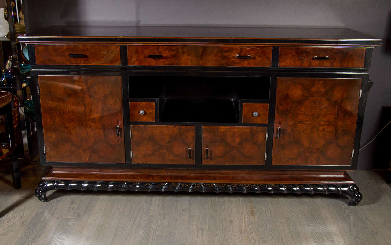 This stunning sideboard features bookmatched burled walnut with black lacquer accents and a inset skyscraper style niche. It rests on a hand-carved reptilian style base. It has five drawers and four spacious cabinets so it provides great storage.
