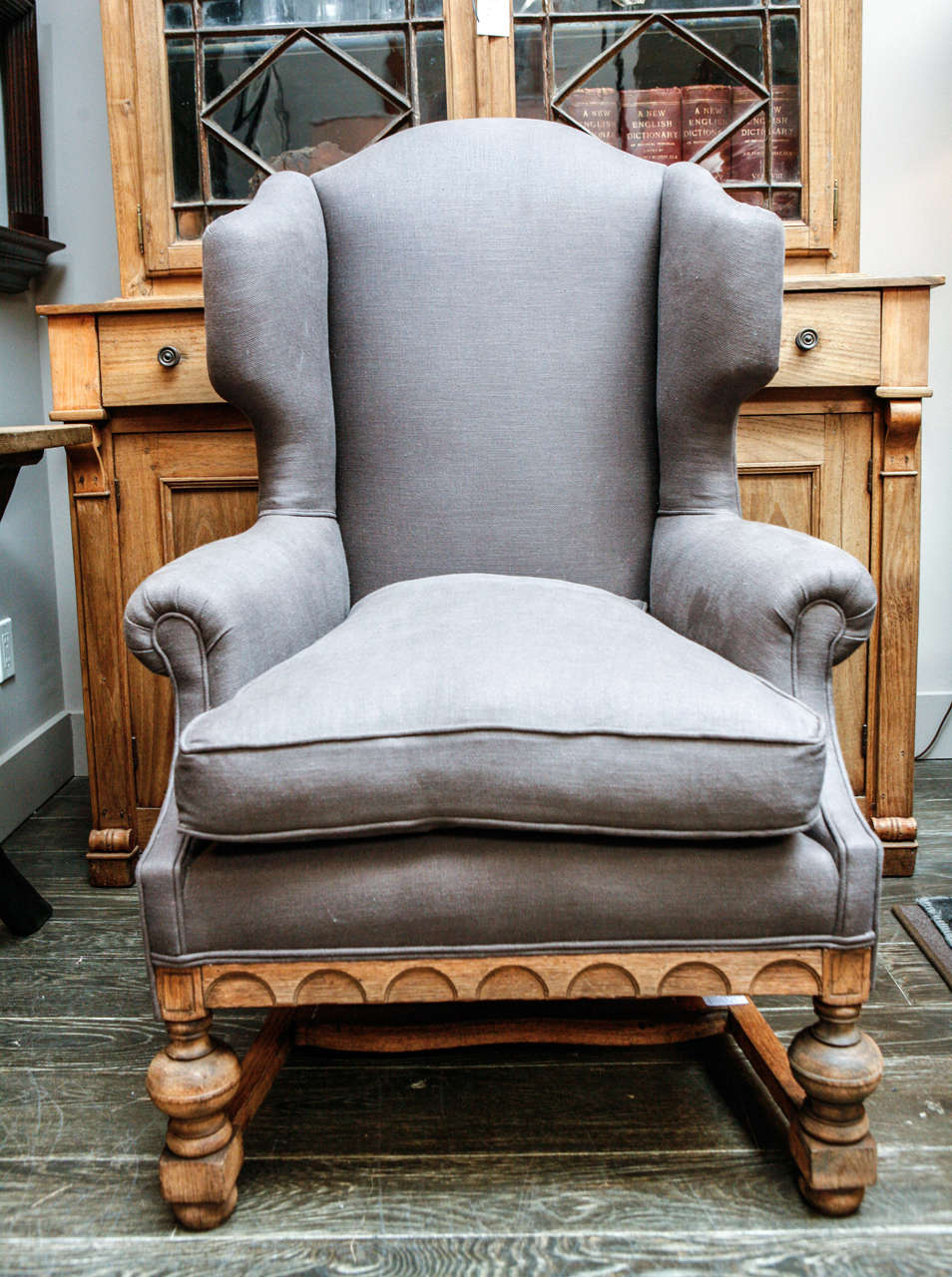 A linen upholstered deep winged chair with out-scrolled arm rests and a carved oak apron and bobbin leg stretcher base