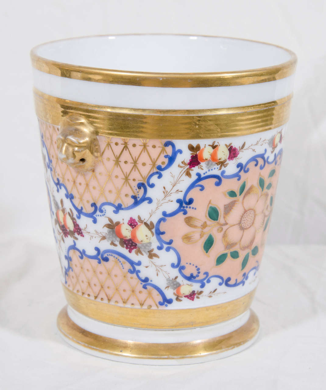 A pair of Paris porcelain cache pots and stands with a design of fruits and flowers painted in a variety of bright colors on a richly gilded peach ground.
On each side are gilded lion's head handles.