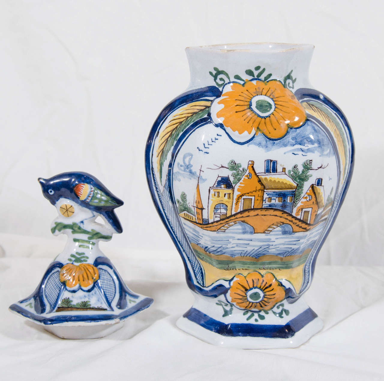 A pair of 18th century Dutch Delft polychrome covered mantle vases. They show a brightly colored village scene with a bridge over a river. The covers have traditional bird finials.