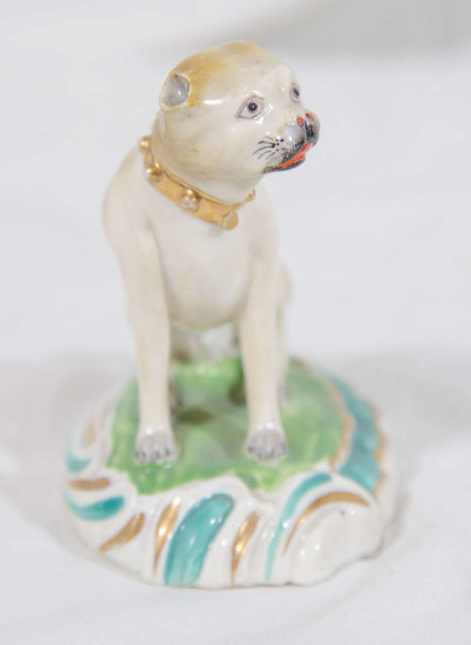 A fine Derby model of a pug seated on a scroll molded base, the pug delicately shaded with beige body, red tongue and nostrils, and black muzzle. The collar picked out in gilt. The base painted pale green and turquoise.