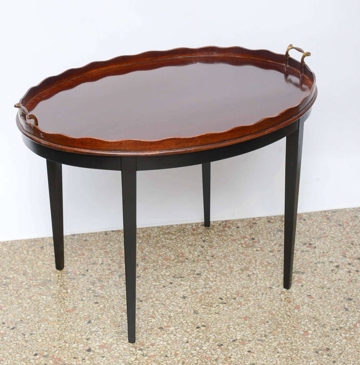 Beautifully executed with scalloped edge and brass handles. The tray is mahogany with cross banding affixed to a satin black stand with tapered legs.  Restored finish.
