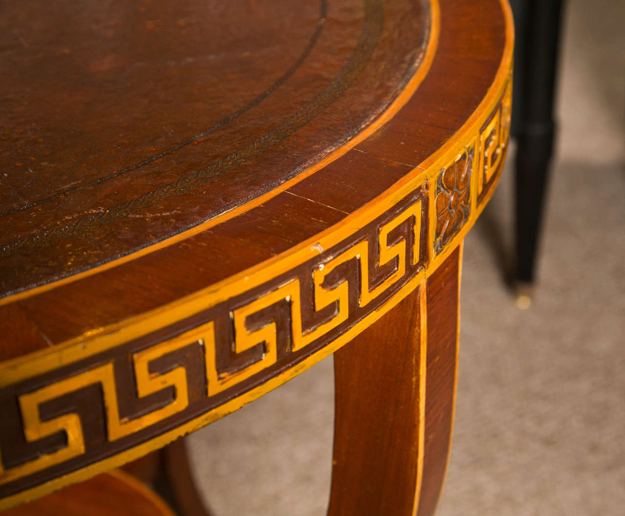 Regency style rosewood gueridon center table, circa 1940s, the circular top with brown leather surface over a narrow frieze decorated with greek key pattern, raised on four splayed legs joint by a small round lower tier, ending in brass caps. By