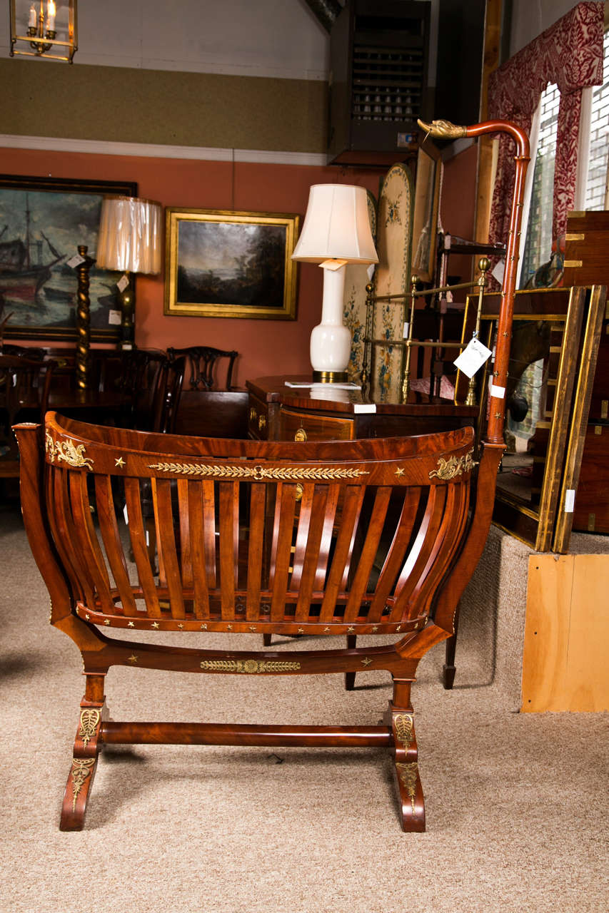 A spectacular French Empire  mahogany baby cradle, mid 19th century, decorated with ormolu mounts, the cradle swings, supported on a double-pedestal base joint by a single stretcher. Finely case bronze mounts throughout. The top terminating in a