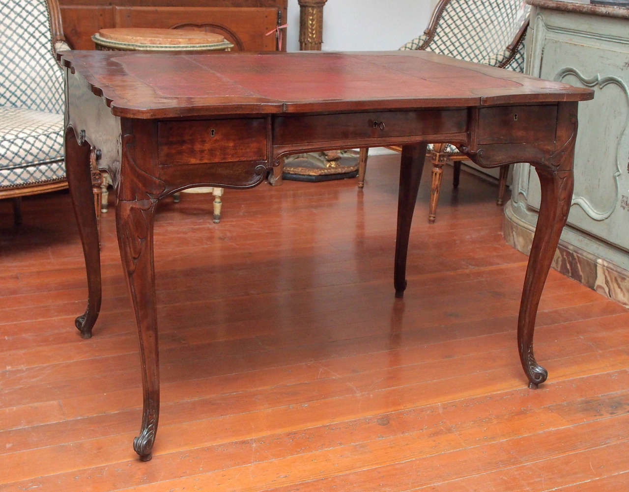 An elegant, well proportioned writing table with tall cabriole legs ending in finely carved snail toe feet, the original, tooled leather and walnut veneered top over three drawers, the apron and front shaped.  This finely made piece has been loving