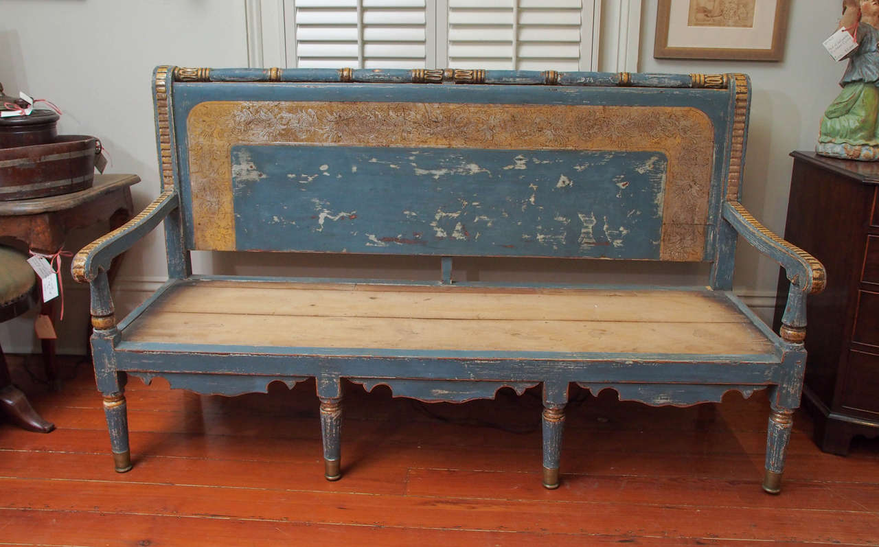 A blue paint and gilt settee or bench on tapered legs and with open arms, the back with incised carving and a turned top rail.  Having a loose cushion, which we show only for informational purposes as it is 