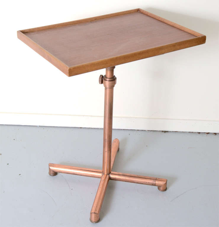 Adjustable wooden table on copper cross base. Folds out so that there are two work surfaces. Marked with Caruelle sticker on bottom of wooden top.
