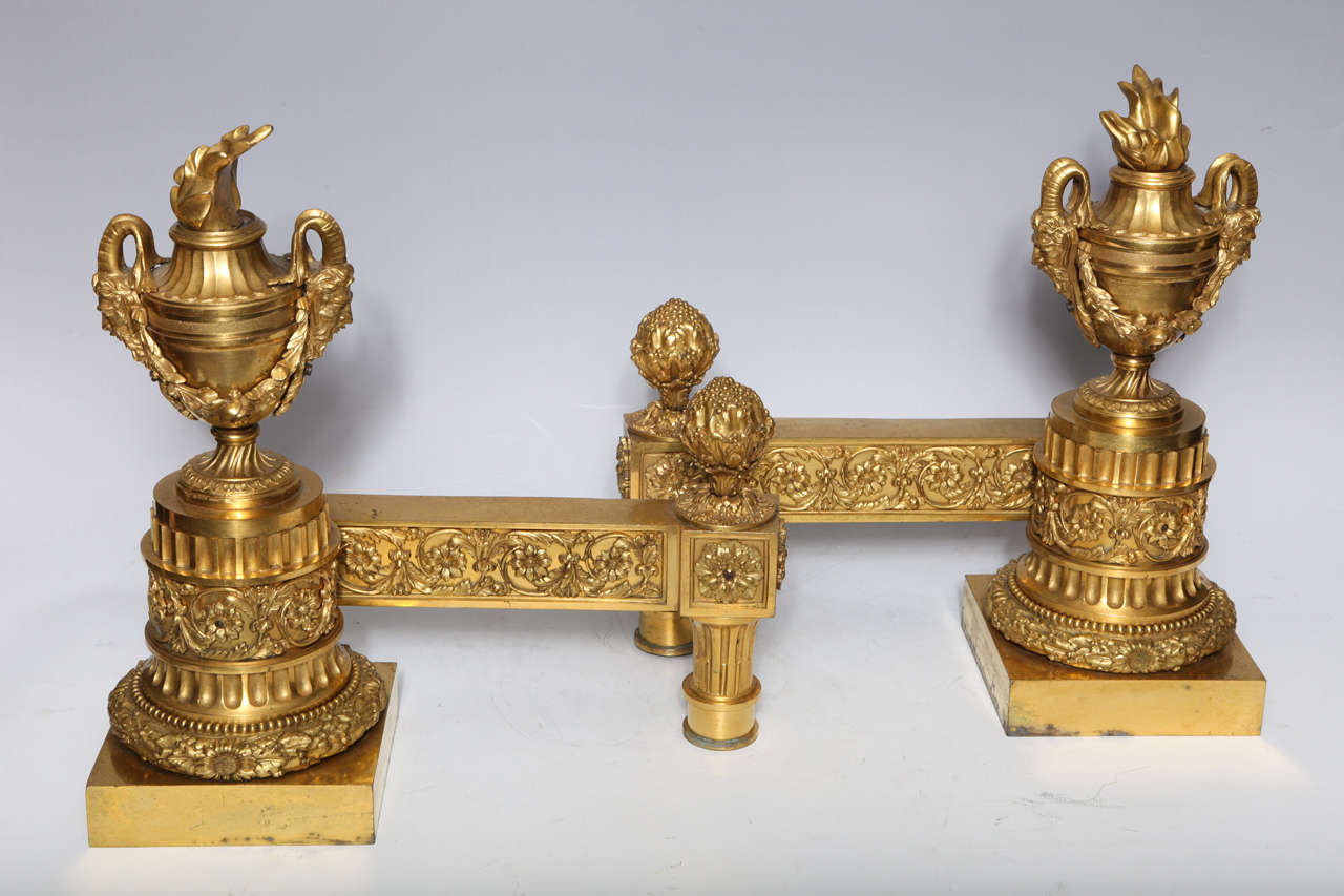 Pair of superb antique French Louis XVI period gilt bronze fireplace andirons/chenets of fine workmanship embellished with neoclassical urns adorned with figural masks, Paris, circa 1780.