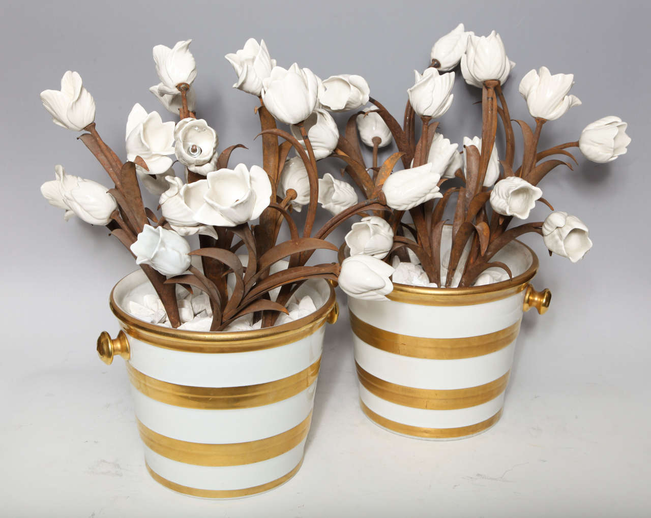 A large and quite unusual pair of antique French Louis XVI style white and gold two handled porcelain buckets filled with white tulips mounted on handmade metal stems, attributed to Jansen Paris, circa 1910.
 