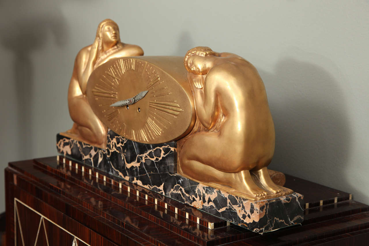 A gilded bronze Art Deco mantel clock by Raoul Eugene Lamourdedieu, (1877-1963), mounted on a portoro marble base, 
flanked by two kneeling nude maidens, signed Lamourdedieu.
Length 24 3/4 inches.