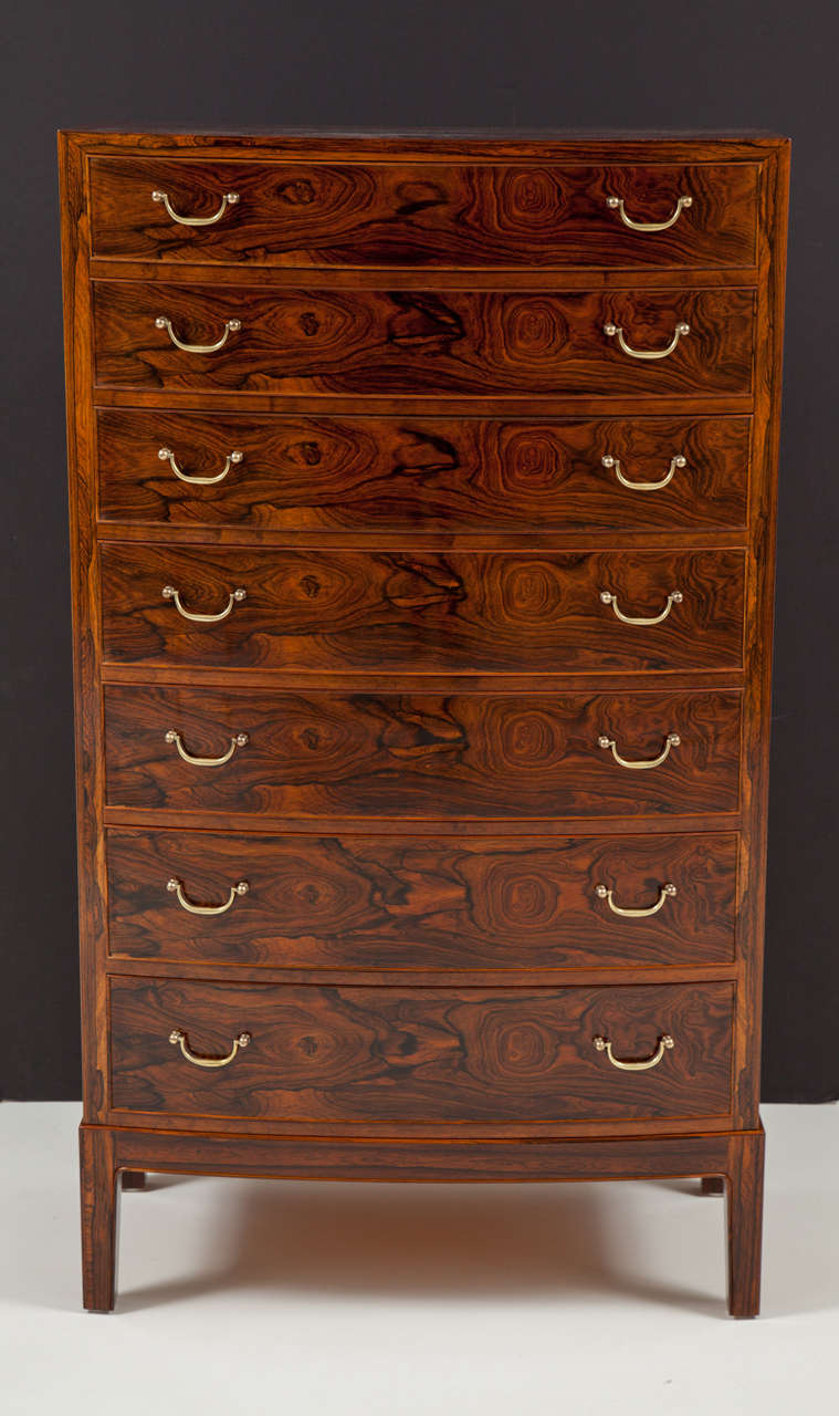 A striking rosewood semainier designed by Ole Wanscher. Born Frederiksberg 1903, Died Charlottenlund 1985.
With a gentle bow front above seven conforming drawers raised on square feet. Brass pulls.

Manufactured for Copenhagen retailer Illums