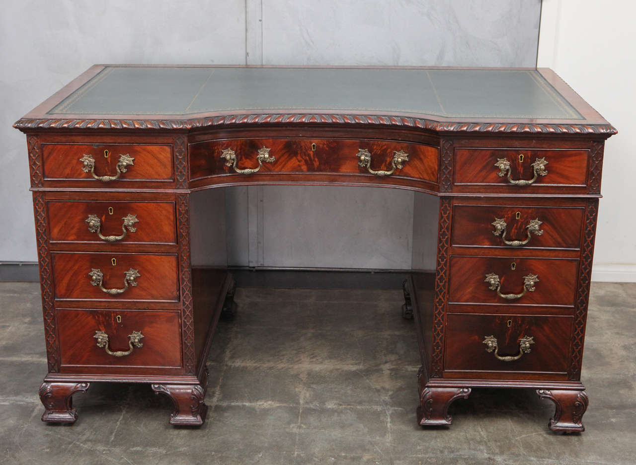 This handsome two pedestal desk is a great example of Chippendale style furniture with incredible craftsmanship and delicate patterns in the flaming of the Mahogany wood. The drawers have decorative brass rosette drop pull handles with inset brass