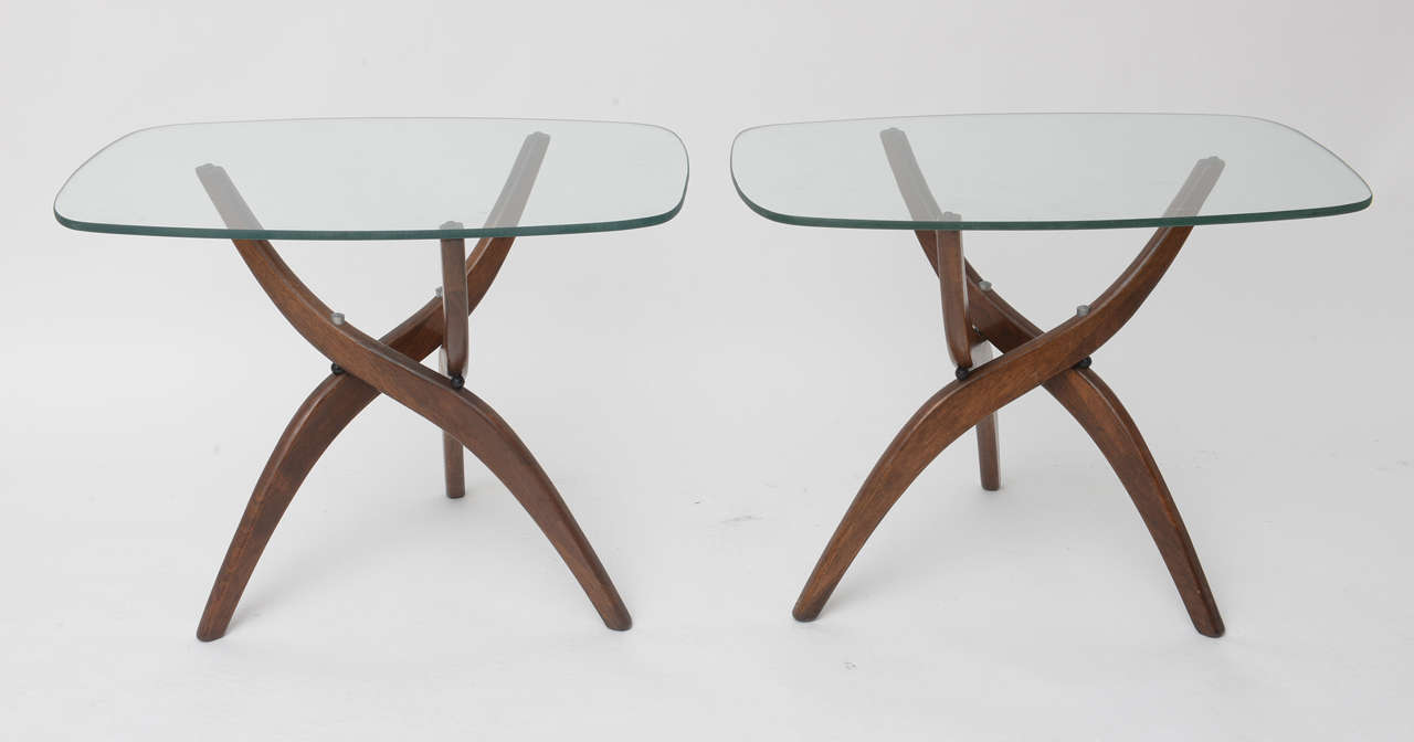 Beautiful period design walnut side tables featuring three crisscrossed legs and  glass tops. Great original condition. Will compliment a mid century sofa.
A cocktail table of this same design is also available; please see our website or feel free