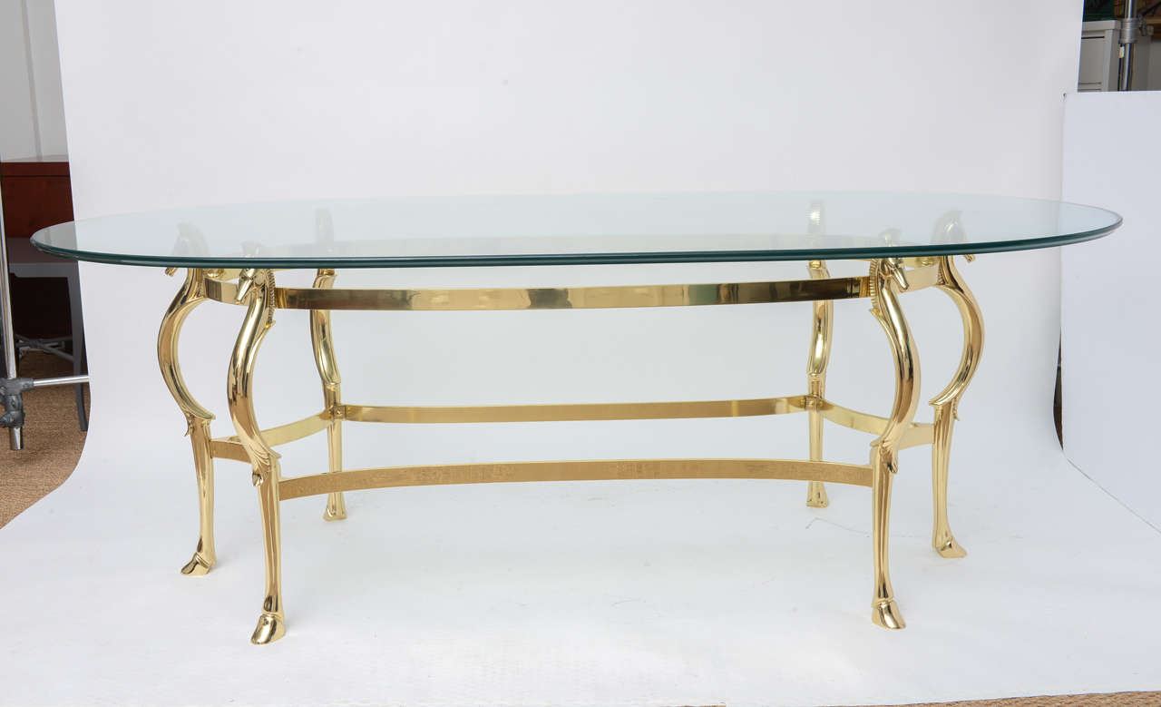 Exquisite polished brass dining table featuring six legs with regal horse heads holding the glass top while terminating with hoofed feet. The execution of the brass horse heads and legs is fantastic. The table is secured by two tiers of framework