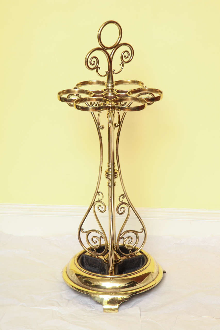 An outstanding curvilinear heavily cast and tubular brass umbrella Stand, with circular carrying handle above a solid cast six aperture holder on tripartite serpentine supports framing scrollwork. The moulded base with three outcurvate feet and