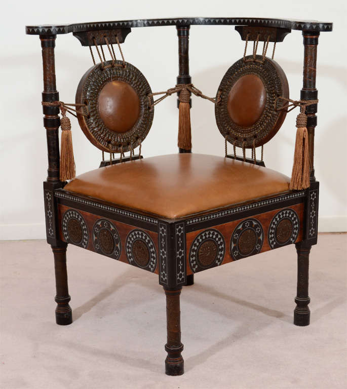 An antique Moroccan influenced corner chair by Carlo Bugatti. The piece is predominantly walnut with inlaid pewter, bone and ebonized wood detailing and hand hammered copper medallions with leather accents.