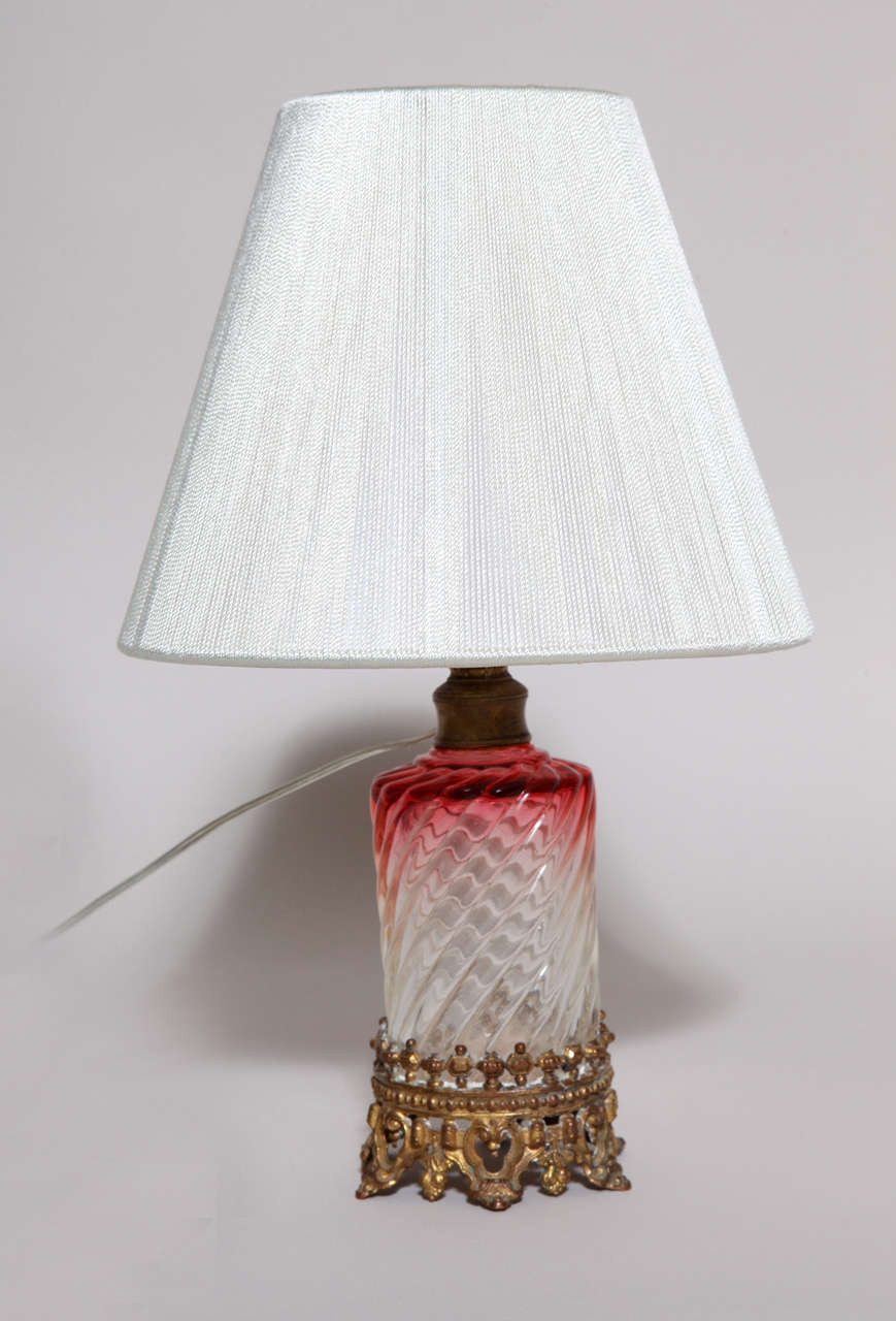 Small cranberry glass table lamp with Baccarat crystal swirl bottle on gilt bronze base.

Measures: 7 1/2''(Height to top of socket) x 12 1/2'' (Overall height) x 3 3/4'' (Diameter of base) x 8'' (Diameter of shade).