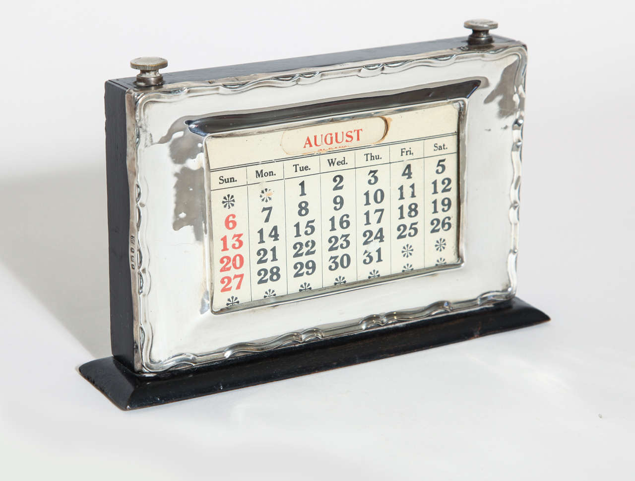 Sterling silver framing the calendar on an ebonized wood frame and base with glass over calendar. There is a wood door in rear for changing months (all cards present).
Hallmarks: 925 silver, Birmingham, 1925, WJM & Co.