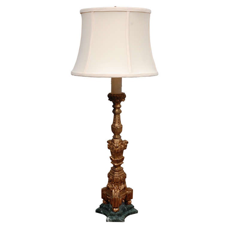 These impressive table lamps are made from a pair of period candle stands on green marble stands. The carved wood pillars are gilded with a reddish tone underpainting. This pair would make a significant impression in a variety of settings. 