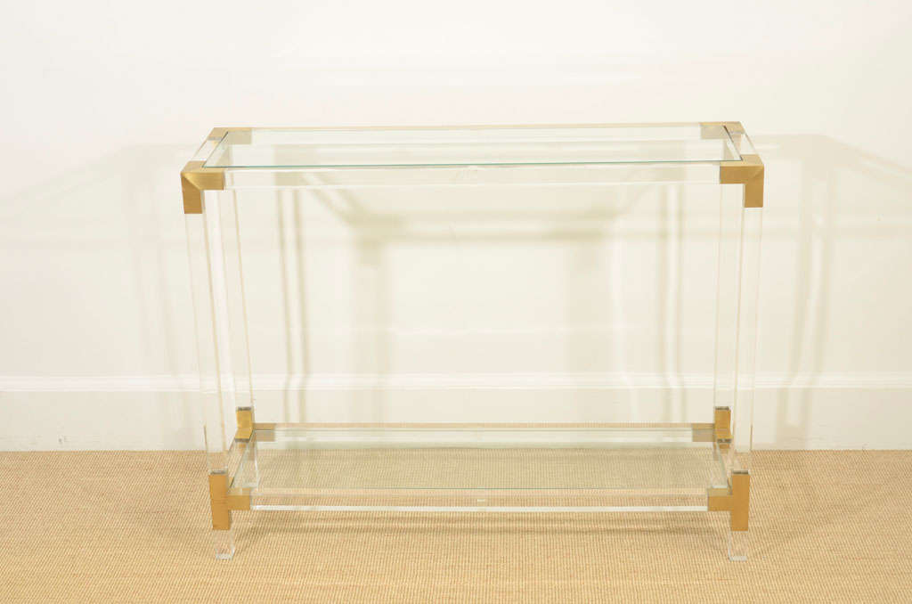 The rectangular body made up of squared lengths of lucite held in brass fitting, supporting two glass shelves.