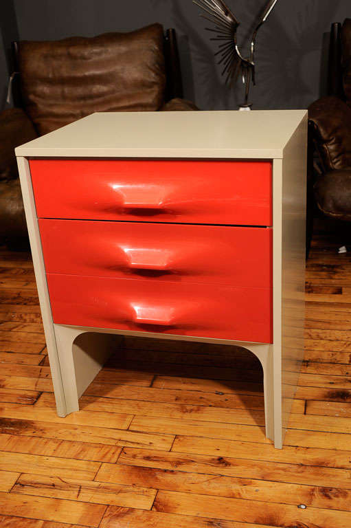 the two drawer nightstand by Raymond Loewy features his signature molded plastic drawer fronts in orange paired with a white cabinet.