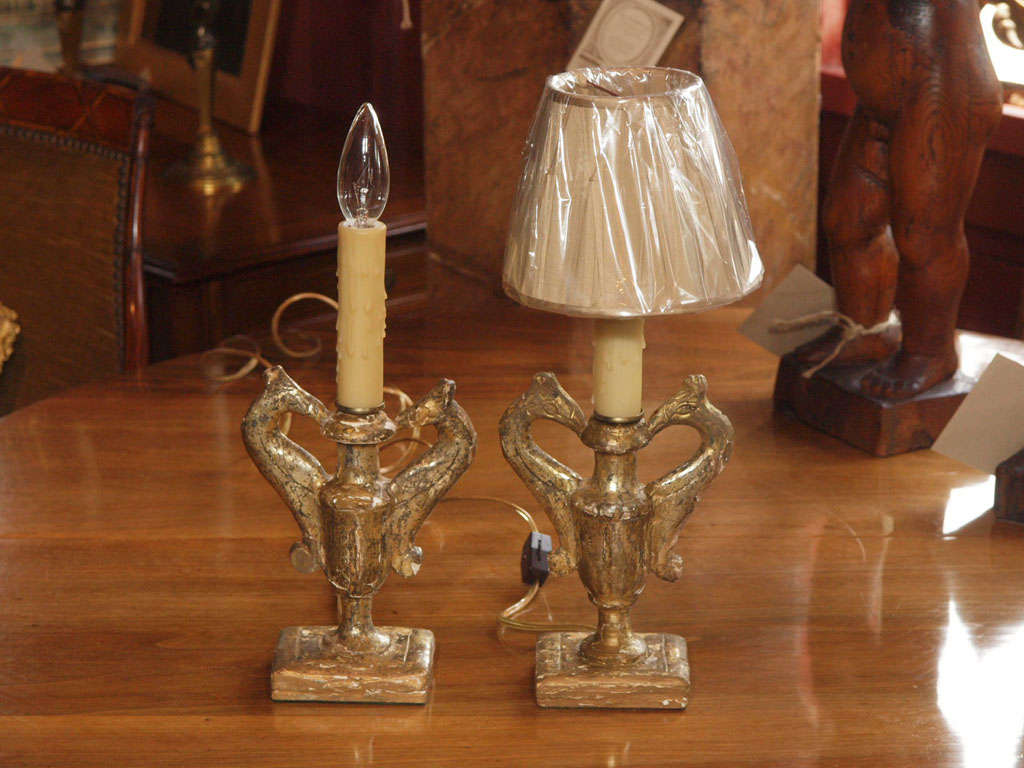 A diminutive pair of gilt urn bases with griffin handles converted into lamps.  The front of the urn is gilded and the back is unfinished.  Bases are weighted. Shades are not included in price. Require a clip on shade