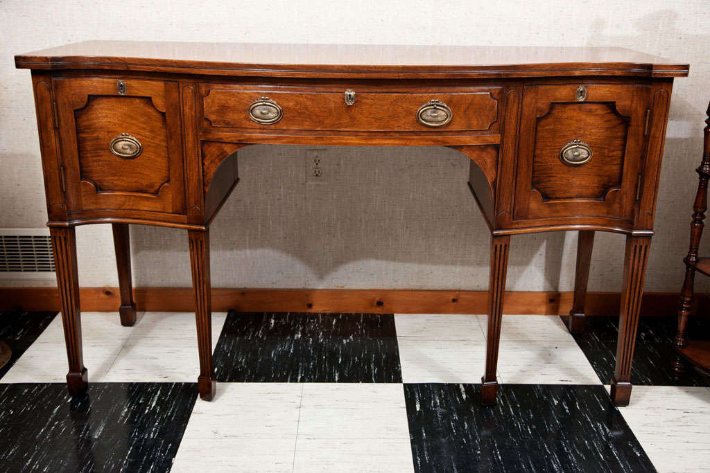 With a center silver drawer flanked by cupboards, this serpentine sideboard, while highly attractive, doesn't at first appear unusual. It is on closer inspection that one is treated to the realization that it is constructed of solid mahogany. Most