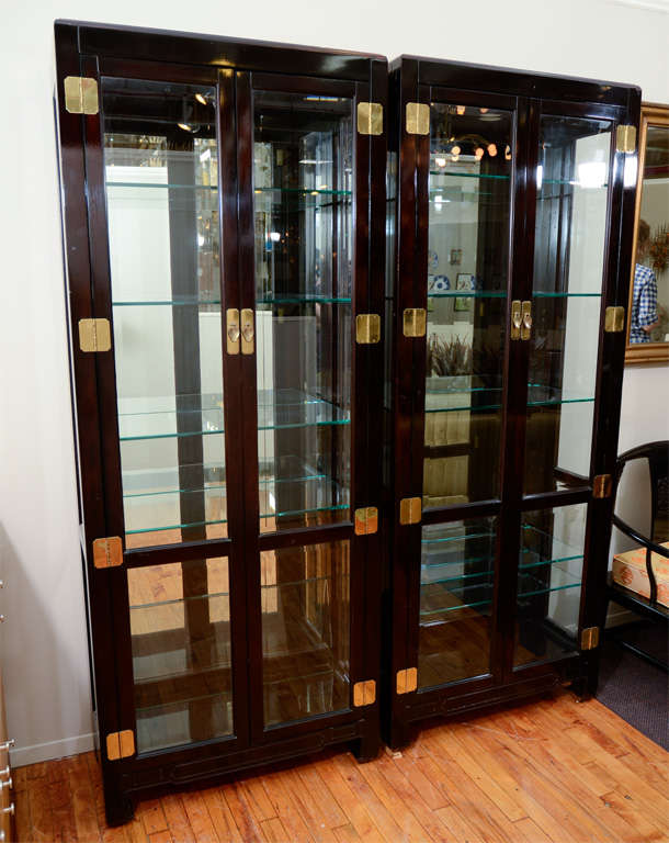 A pair of Henredon vitrines with black lacquered finish and brass hardware. The interior of each has adjustable glass shelves backed by mirror.<br />
<br />
Reduced From: $5,200