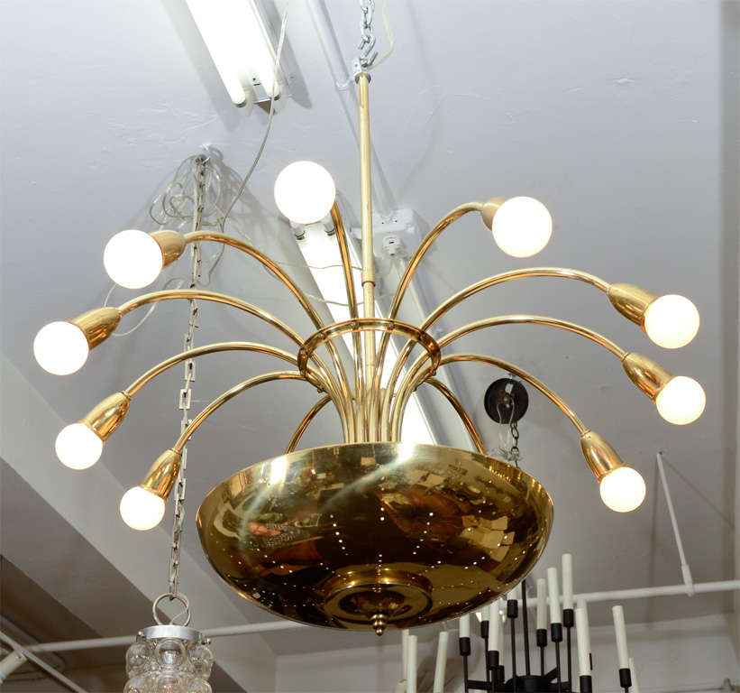 A fountain form chandelier, with 12 bulbs at the end of arching brass arms, with four additional bulbs within the half-globe perforated brass shade. Good vintage condition, with age appropriate wear.

4426.