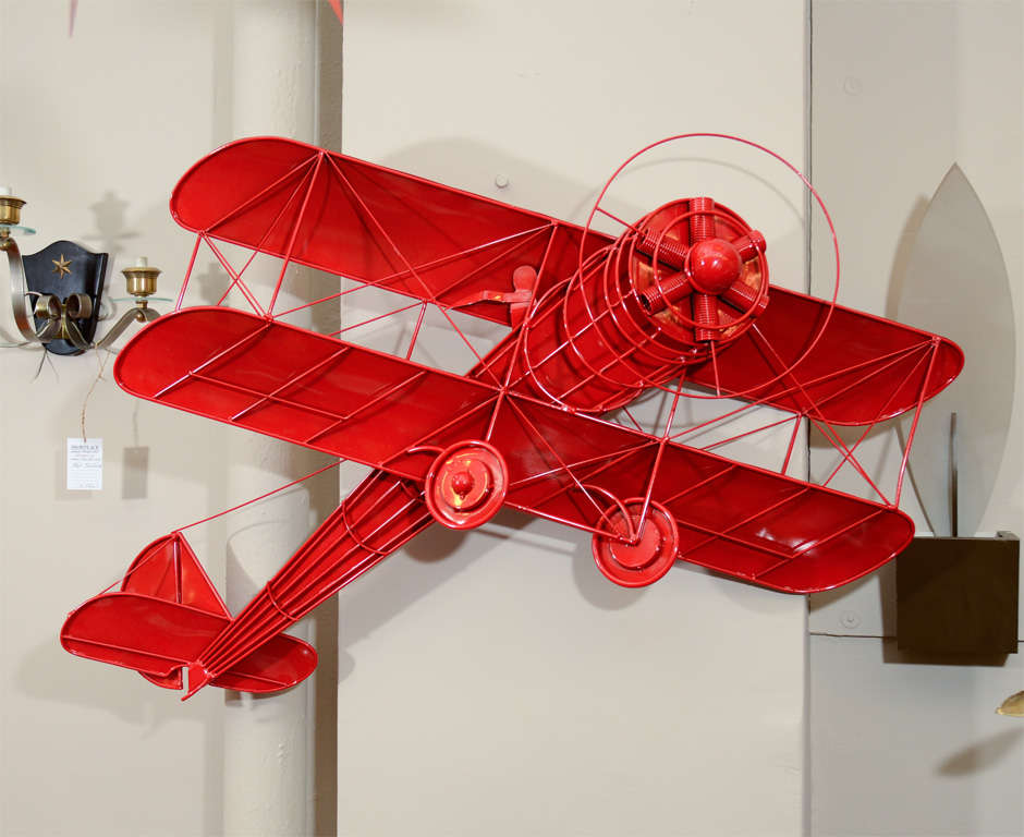 Three dimensional wall mounted metal sculpture in the form of a vintage biplane with pilot. Powder-coated in bright red.