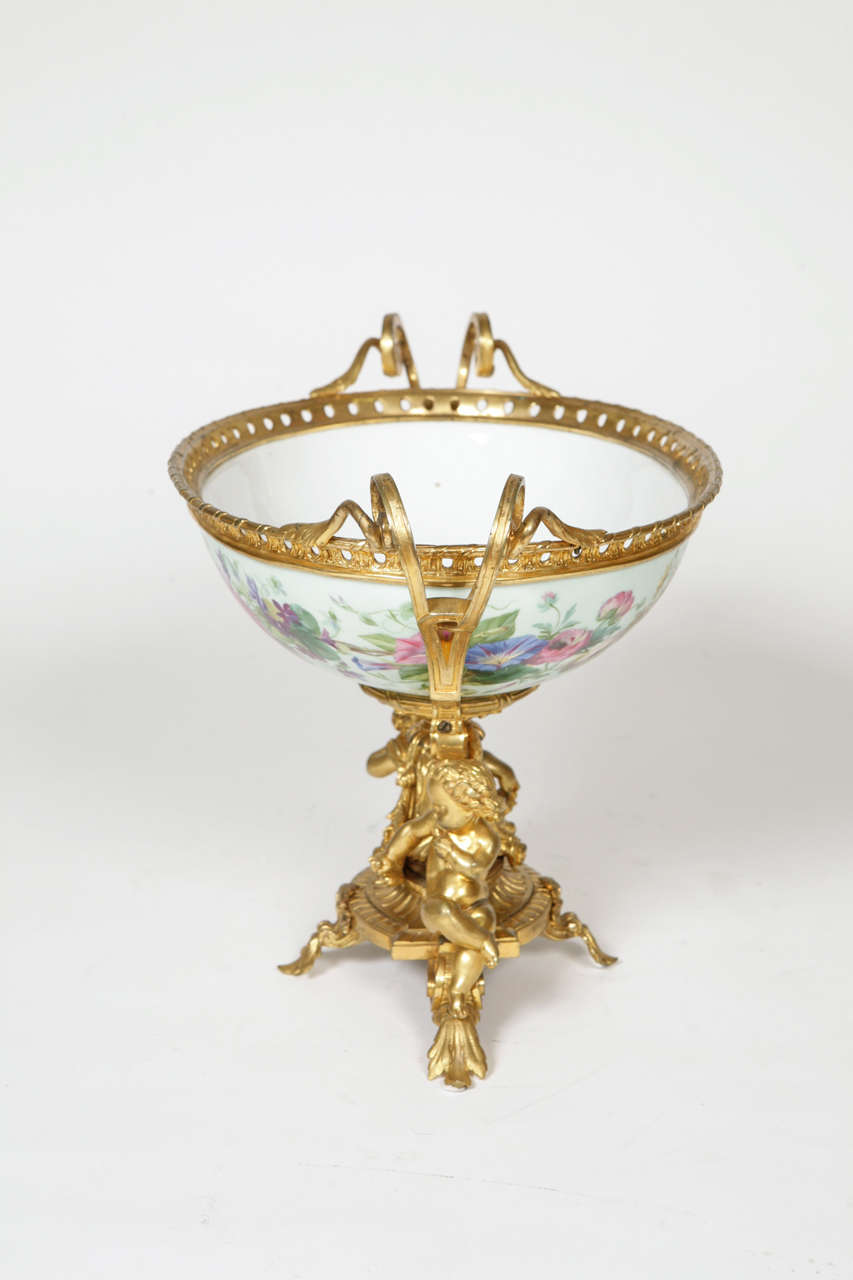 The porcelain body finely painted with polychrome flowers on a light green ground; featuring ormolu twin-handles and seated cupids to the base.