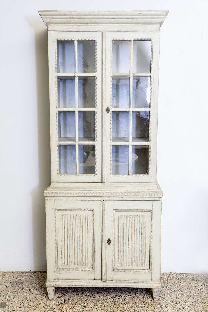 Antique period Swedish Gustavian cabinet in two sections in a light gray-green colour. The upper part has beaded trim and original glass. The lower part has raised panel doors with carved groves and beaded trim. Original locks and hinges.