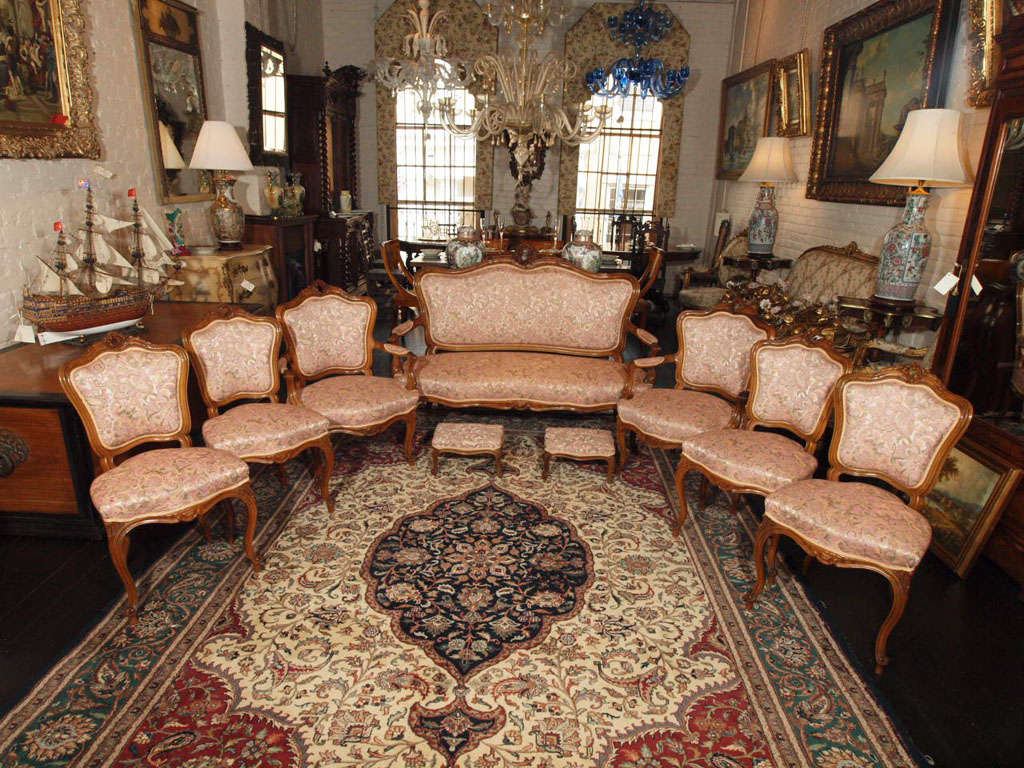A 9 piece Louis XV style parlor suite including a settee, 2 arm chairs, 4 side chairs and 2 foot stools. Walnut frame with stylized floral upholstery. The settee is 58