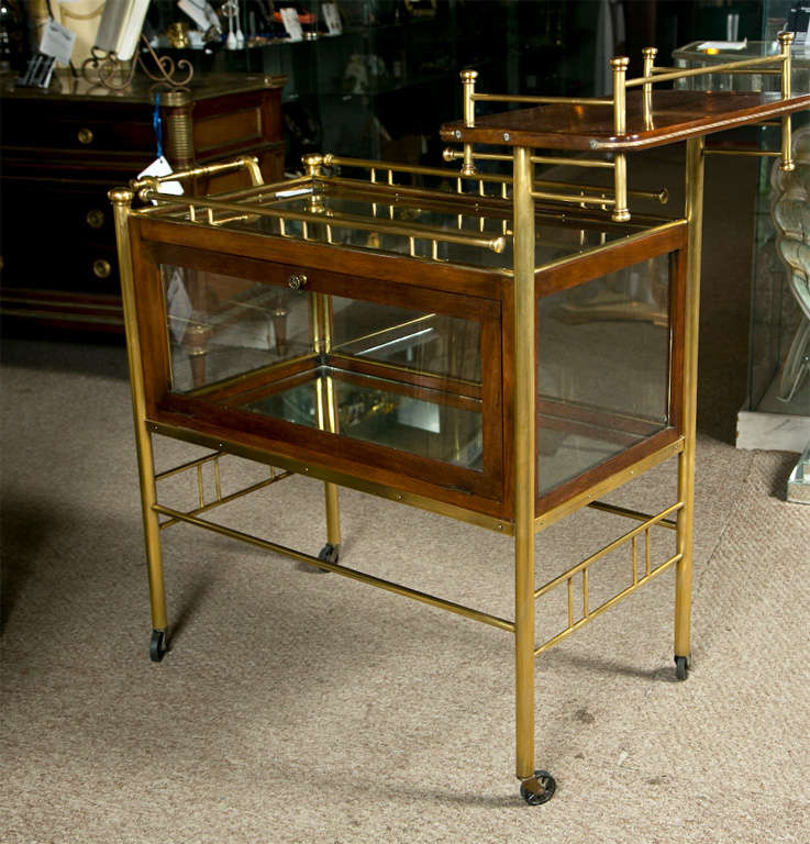 A very nice custom quality mid-century brass showcase tea cart - serving wagon. The rolling casters leading to a group of four brass columns, having an undercarraige, supporting a showcase top with an upper tier. Both the showcase and top are