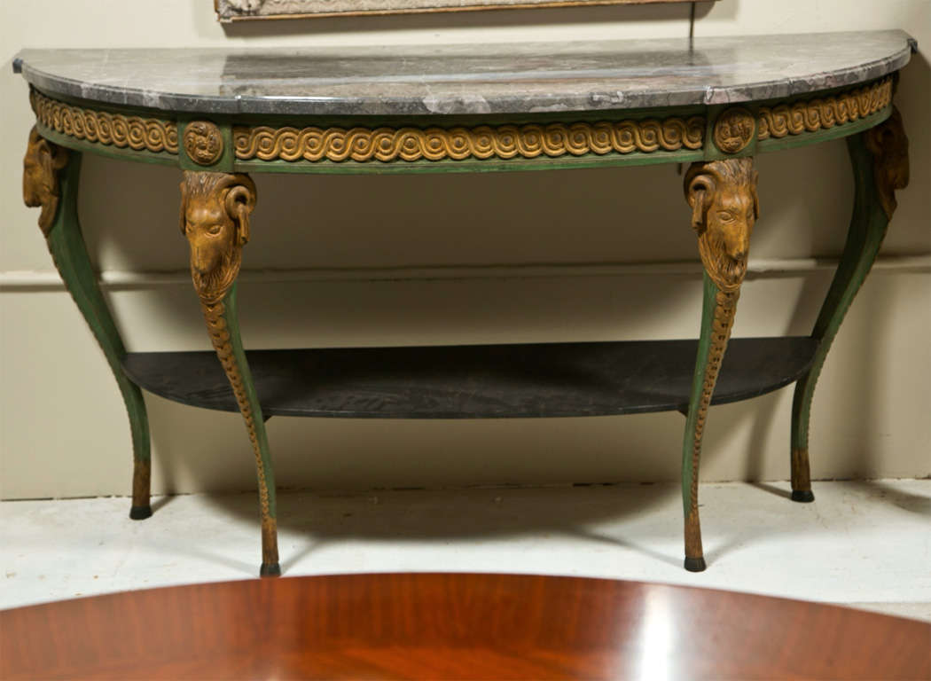 French Neoclassical style demilune console table, the half-moon gray marble atop a green-painted and parcel-gilt frieze decorated with annulated pattern, raised on four cabriole legs each headed by ram's head, joint by a lower tier.
