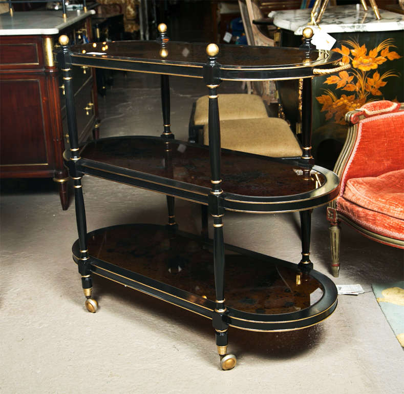 French ebonized and parcel-gilt bar cart, circa 1940s, three tier of glass top oval shelves supported by spindle uprights, raised on wheels. By Jansen.