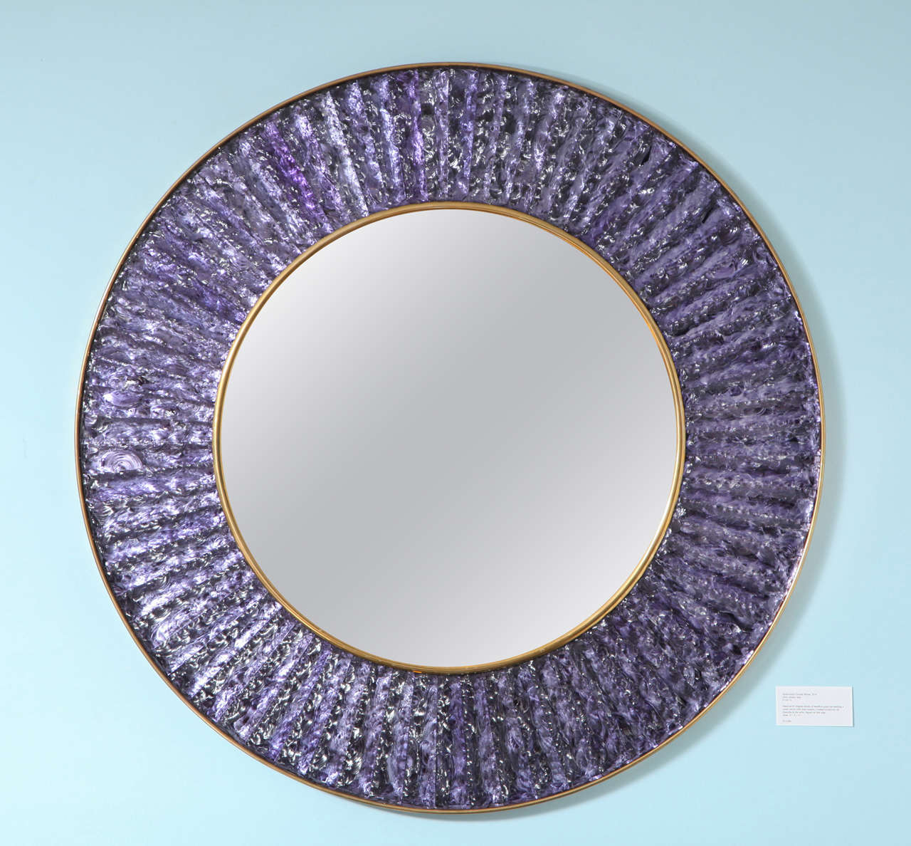 Contemporary wall mirror of hand-cut and chipped chunks of amethyst glass. Arranged in a circle around a central mirror with brass mounts. Beautiful studio made piece created exclusively for Donzella. Signed on side edge.