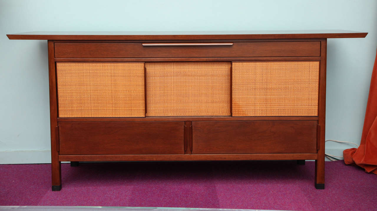 Rare sideboard by Edward Wormley for Dunbar. Overhanging slab walnut top. Mahogany case with three drawers, and three sliding doors that open to reveal more storage. Bentwood pulls and leather wrapped feet. Door fronts with rattan faces and cloth