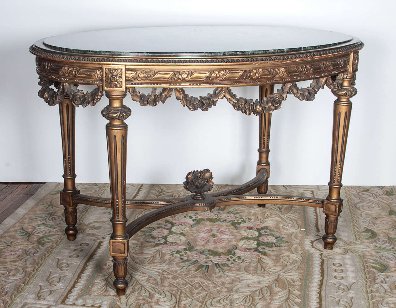 Highly ornate, hand-carved gilded oval wooden table with decorative swags and fluted legs in Louis XVI style. Green marble top in excellent condition with no breaks or damages. This item can be seen at our 149 Madison Ave. location in Manhattan.