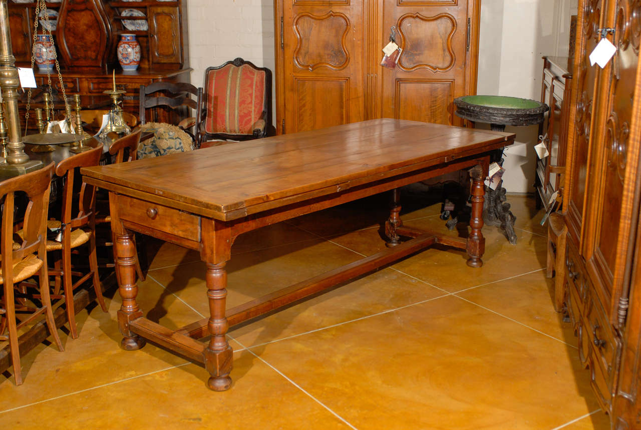 A 19th century French fruitwood farm table with pull out leaves, drawer and stretcher. The total length with leaves pulled out 139.5