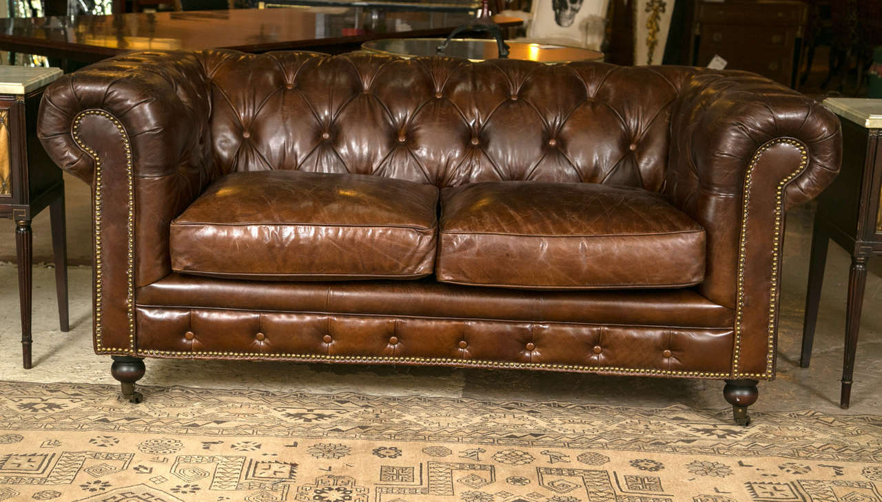 A finely distressed pair English Chesterfield sofa settee. On a bun foot on a caster supporting a finely worn leather Chesterfield love seat. The bottom covering of burlap material. Can purchase one if only one is needed. 2661 ZhXX.