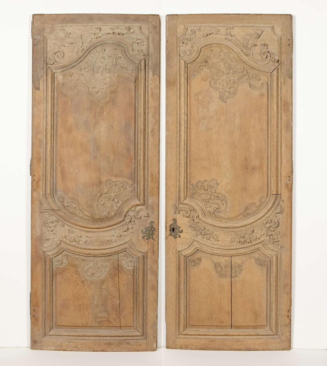 These beautifully hand-carved armoire doors are from the French Regence period (1715-1723). The front sides have been stripped at some point in their history, while the backs are painted in a cream color. Each door has a very subtle bow
