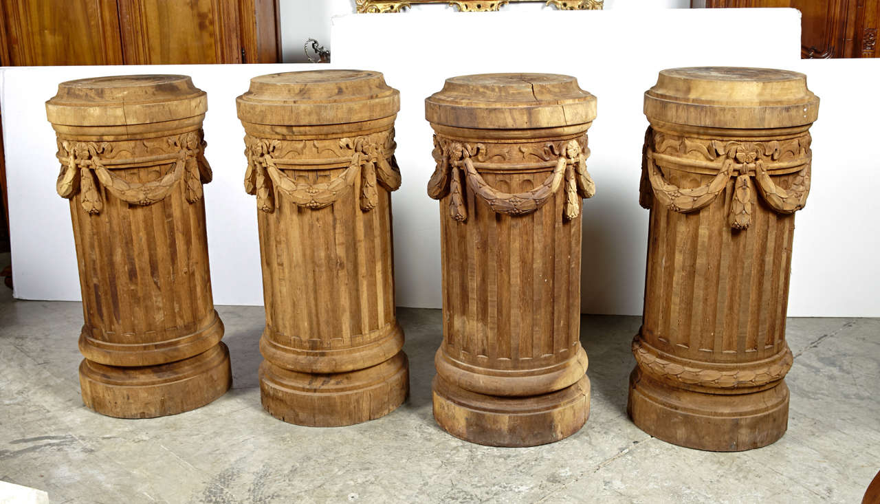 These four Louis XVI style fluted wooden column pedestals have garlands of beribboned swags with husk motifs .  They are adaptable to a variety of uses, from holding artwork and sculptures to planters with overflowing vines or flowers.  Each