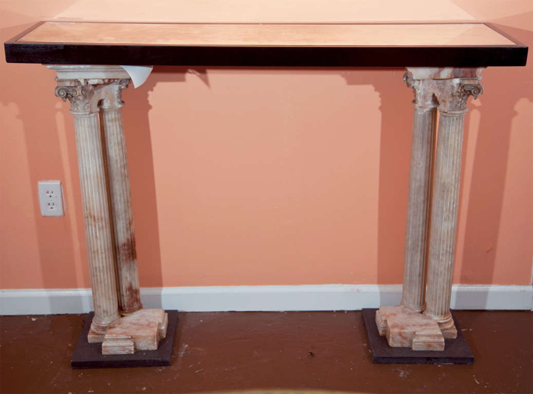 Neoclassical style console table, circa 1940s, ebonized top with smokey glass inset, supported by beautiful alabaster column pedestals, raised on squared block bases.