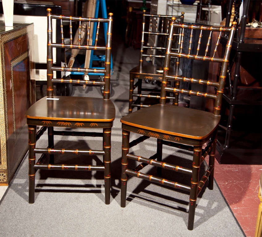 Pair of English faux bamboo dining chairs in the taste of chinoiserie, overall ebonized with parcel-gilt painting.