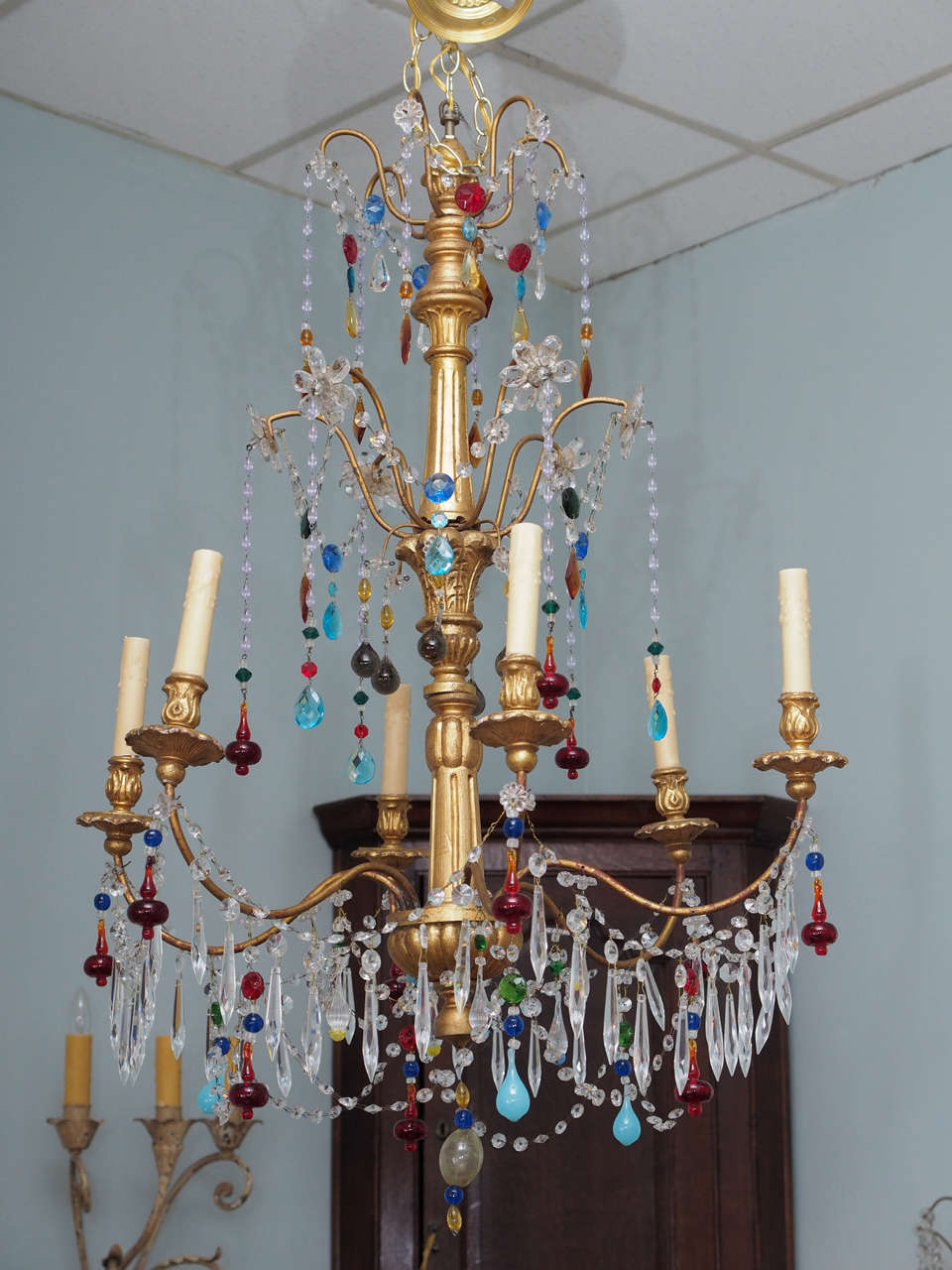 This elegant jewel of a Genovese chandelier is embellished with brightly colored and opaline Murano glass drops as well as clear crystals and was created in Italy, circa 1920. There is a carved giltwood central shaft with an upper finial and six